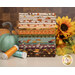 A stack of the fabrics included in The Awe of Autumn FQ set, with flowers and pumpkins and leaves and thread.