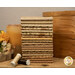 A stack of the nuetral fabrics included in the Toasted FQ Set, with boxes and a candle and flowers and a book and thread.