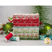 A stack of fabrics included in the Sugarberry collection, with ornaments and a tree and thread.