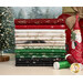 A stack of Christmas fabrics included in the Believe collection, with a sled and trees and Santa and thread.