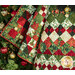 A festive quilt with red, green, and white diamond patterns draped over a Christmas tree decorated with ornaments.