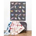 One bird themed Jelly Roll quilt, hung on a white wall; below it, a coordinating gray couch has two Jelly Roll quilts draped over it.