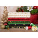 A stack of the holiday-themed fabric included in the Holiday Blenders collection by Timeless Treasures Fabrics, with a basket and a candle and ornaments and thread.