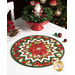 The completed table topper, colored in red and green fabrics from the Yuletide Traditions collection, staged on a white table with coordinating holiday decor including a santa, garland, and Christmas tree.