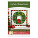 Front cover of the Log Cabin Christmas Wreath pattern, showing the completed projects staged above a green armoire decorated with glittering cotton snow, presents, and a Christmas tree.