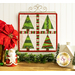 The completed Foundation Paper Piecing Series 2 project for December, an arrangement of four dynamic Christmas trees in red, green, and white fabrics, staged on a rustic wooden tabletop from a craft hanger with coordinating decor.