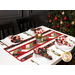 The completed Venice Table Runner colored in black, red, cream, and green fabrics from the Starberry collection by Moda Fabrics, staged on a white table surrounded by coordinating tableware, cloth napkins, and a decorated Christmas tree with a candle as the table centerpiece.