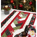 An angled shot of the patchwork of the table runner staged on a white table surrounded by coordinating tableware, cloth napkins, and a decorated Christmas tree, demonstrating fabric and piecing details.