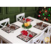 The four completed placemats staged on a white table set with clear plates and coordinating cloth napkins, holiday decor, glasses, and a decorated Christmas tree peeking into the frame.