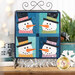 The completed Foundation Paper Piecing Series 2 project for January, an arrangement of four festive snowmen in aqua, navy, and white fabrics, staged on a rustic wooden tabletop from a craft stand with coordinating decor.