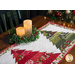 A close up on the table runner, showing three of the pieced patchwork trees beside two lit candles, encircled by a garland.