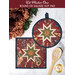 Two quilted hot pads, one round and one square, featuring a star pattern in red, green, and cream next to a wooden spoon and flowers.