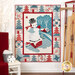 The completed Winter Night in Snowtown Quilt colored in red, white, and blue winter fabrics, hung on a white paneled wall and bordered by coordinating decor.