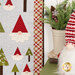 A close up on the right edge of the quilt, demonstrating fabric, laser shape, border, and binding details. A holiday gnome and coordinating decor sit on a green counter on the right edge of the frame.