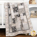 A patchwork quilt in neutral tones draped over a crib, featuring nature-inspired patterns.