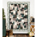 A quilt with a patchwork design in muted tones, displayed on a wall with decorative elements nearby.