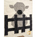 A super close up on a patchwork lamb behind a fence, showing print and piecing details as well as top quilting details. 