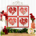 The completed Foundation Paper Piecing Series 2 project for February, an arrangement of four hearts in red, pink, and white fabrics, staged on a rustic wooden tabletop from a craft stand with coordinating decor.