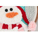 Close-up of a textile snowman with a red and white striped scarf, orange carrot nose, and black buttons.