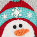 Close-up of a cheerful snowman with a red hat, turquoise accents, and white snowflake decorations.