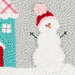 A cheerful snowman with a pink and red hat stands next to a teal house on a grey background.