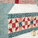 Close-up of a quilt featuring various patterns in red, blue, and cream colors.