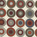 A fabric pattern featuring circular motifs in red, gray, and brown on a cream background.