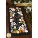 The completed Snowman Lane Flannel Table Runner, colored in vibrant Woolies Flannels, staged on a dark wooden table. A snowy tree peeks into frame and a golden banner at the top reads Laser Cut Flannel.