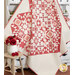 A red and cream quilt draped over a white cabinet filled with flowers next to a floral vase on a stool. 