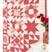 A vibrant red and cream quilt with star patterns hangs on the wall, next to a vase of roses.