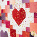 A close up on a bright red patchwork heart block, showing piecing, layout, fabric, and top quilting details as the gold metallic heart accents leap off the colorful fabrics. 