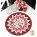 A round table topper with a bursting star design in red, pink, and white fabrics featuring valentine motifs placed on white table next to flowers and glasses. 