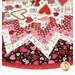 Angled view of table topper featuring a patchwork design of valentine fabrics in black, cream, pink and red.