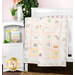 A colorful quilt with alphabet squares hangs over a crib, beside a white cabinet and plant.