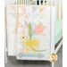 A pastel quilt featuring a yellow bird on wheels and a pink tulip, hanging in a baby crib.