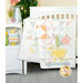 A colorful quilt featuring a yellow chick and tulip design draped over a crib beside a decorated shelf.