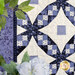 A close-up of a quilt featuring intricate patterns in shades of blue and cream, surrounded by greenery.