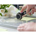 A hand using a rotary cutter on a cutting mat with yellow paper and flowers in the background.