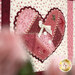 A heart-shaped quilt patch in shades of pink, adorned with buttons, ribbon, and decorative stitching.