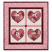 A quilt depicting four heart patterns in pink and red, framed by a floral design, with embellishments isolated on a white backgroound