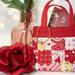 A close up on a single Tiny Tote Bag holding a $25 gift card, staged with a rose and demonstrating fabric and top quilting details as well as showing off a golden heart shaped charm that says 