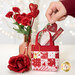 A model inserts a gift card into one of the Tiny Tote Bags, staged with roses and red heart decor.