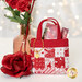 A single Tiny Tote Bag holding a $25 gift card, staged with a pink vase, a rose and demonstrating fabric and top quilting details as well as showing off a golden heart shaped charm that says 