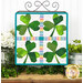 The completed Foundation Paper Piecing Series 2 project for March, an arrangement of four shamrocks in green, rainbow, and white fabrics, staged on a rustic wooden tabletop from a craft stand with coordinating decor.