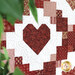 A quilt featuring a prominent red heart design surrounded by various patterned fabric squares.