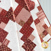 A quilt featuring a geometric patchwork of red and white fabric patterns.