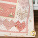 Up close of a pink and cream children's quilt featuring bunnies, hearts, and loving phrases draped over a crib