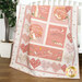 A pink and cream children's quilt featuring bunnies, hearts, and loving phrases draped over a crib