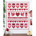 A patchwork quilt featuring red and pink hearts, flowers, and birds arranged in a pattern on a white background surrounded by coordinating decor.