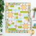 A colorful quilt featuring star patterns in yellow, green, and white, with floral borders and biblical text.